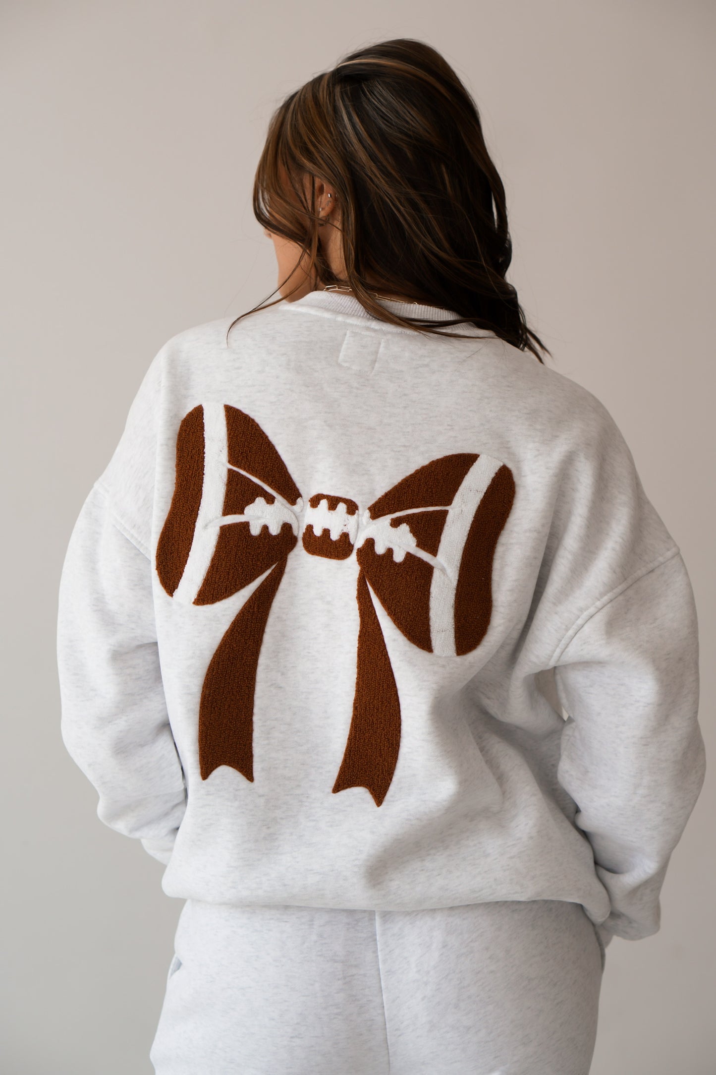 An up close of the back of the sweatshirt that has a big bow on it with football pring
