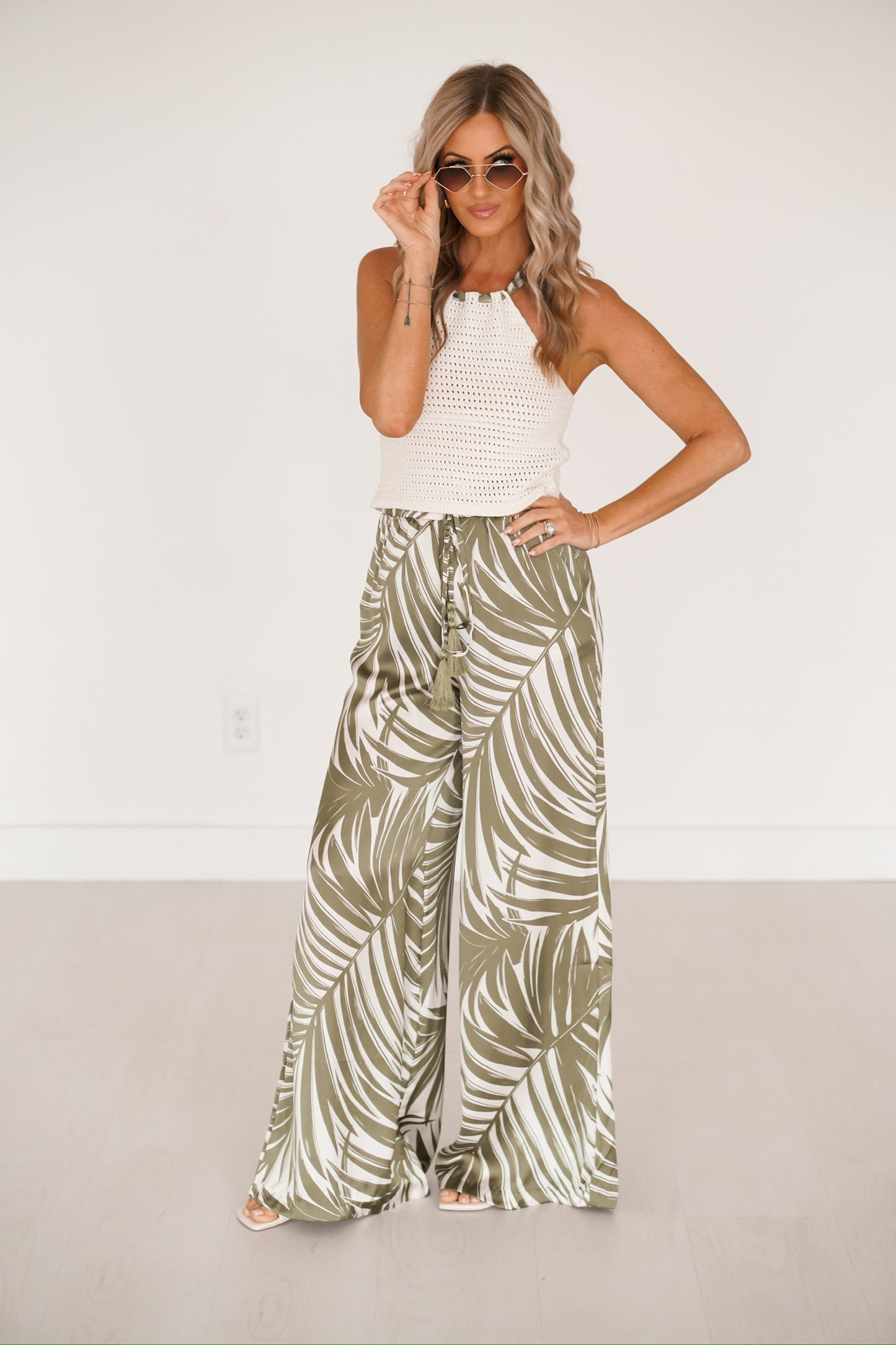 blonde headed girl standing against a white wall wearing a knitted creme palm print top
