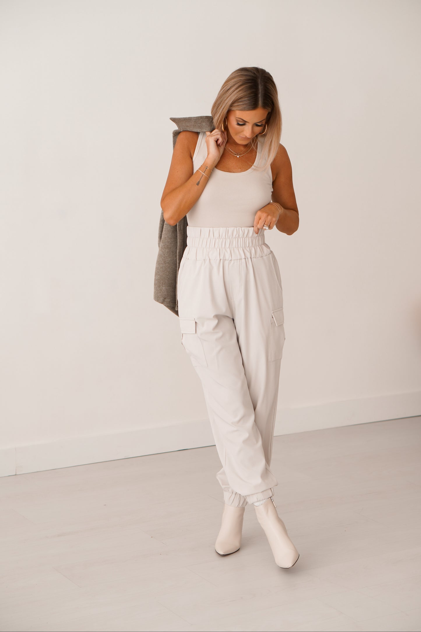 Blonde girl wearing cream cargo joggers holding green shacket over shoulder.
