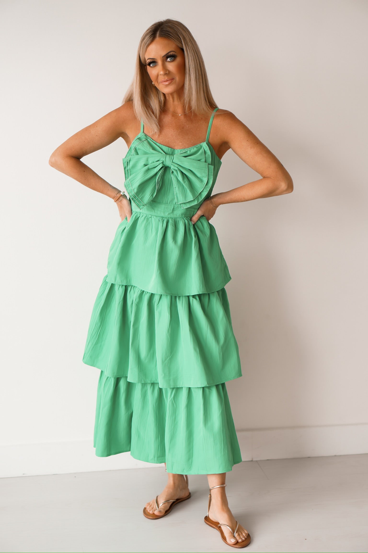 girl standing with her legs crossed wearing a green long bow dress with sandals