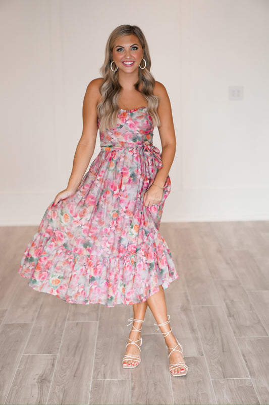 blonde headed girl standing against a white wall wearing a floral long dress