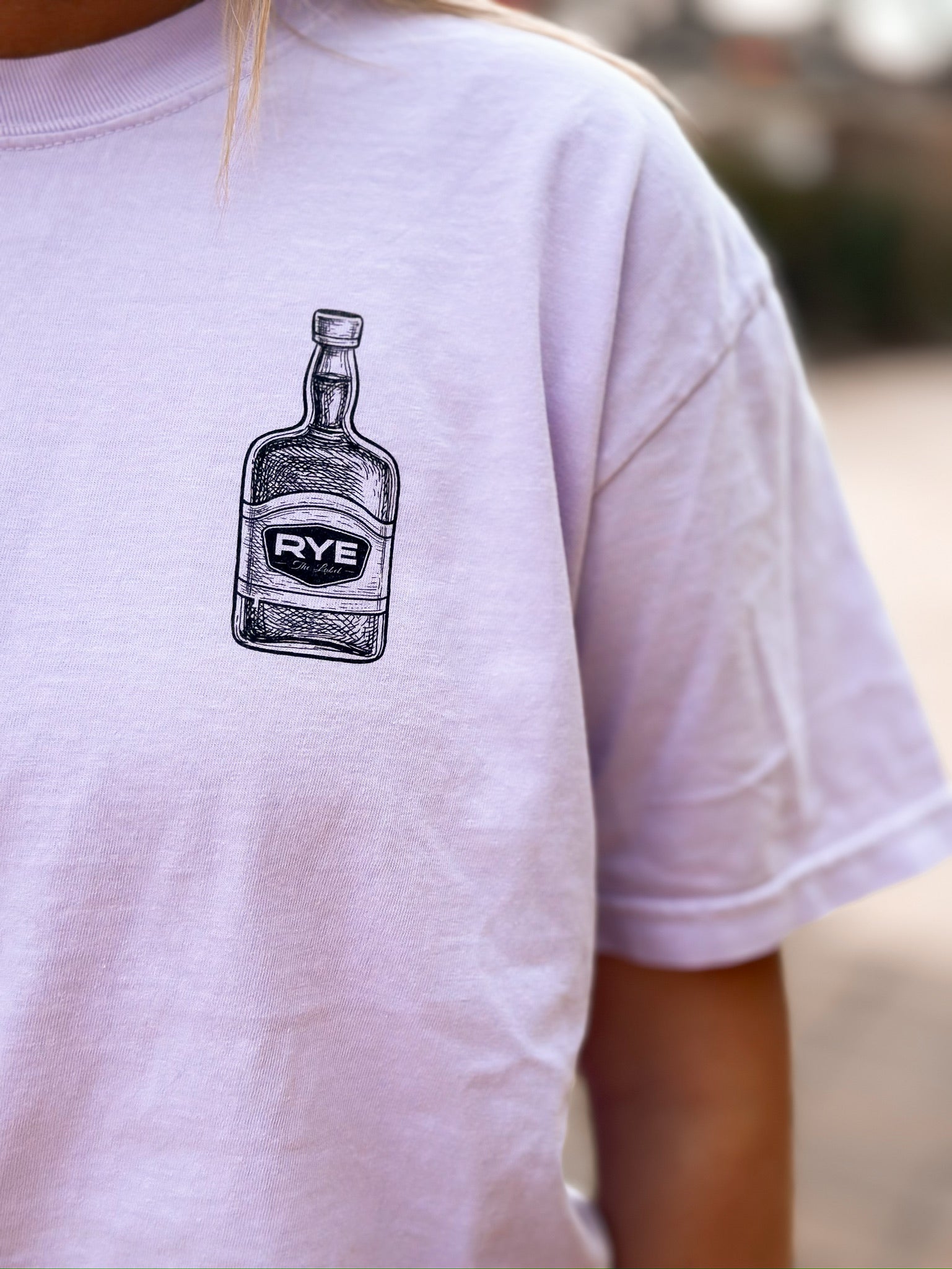 Up close picture of purple shirt with RYE bourbon bottle on it. 