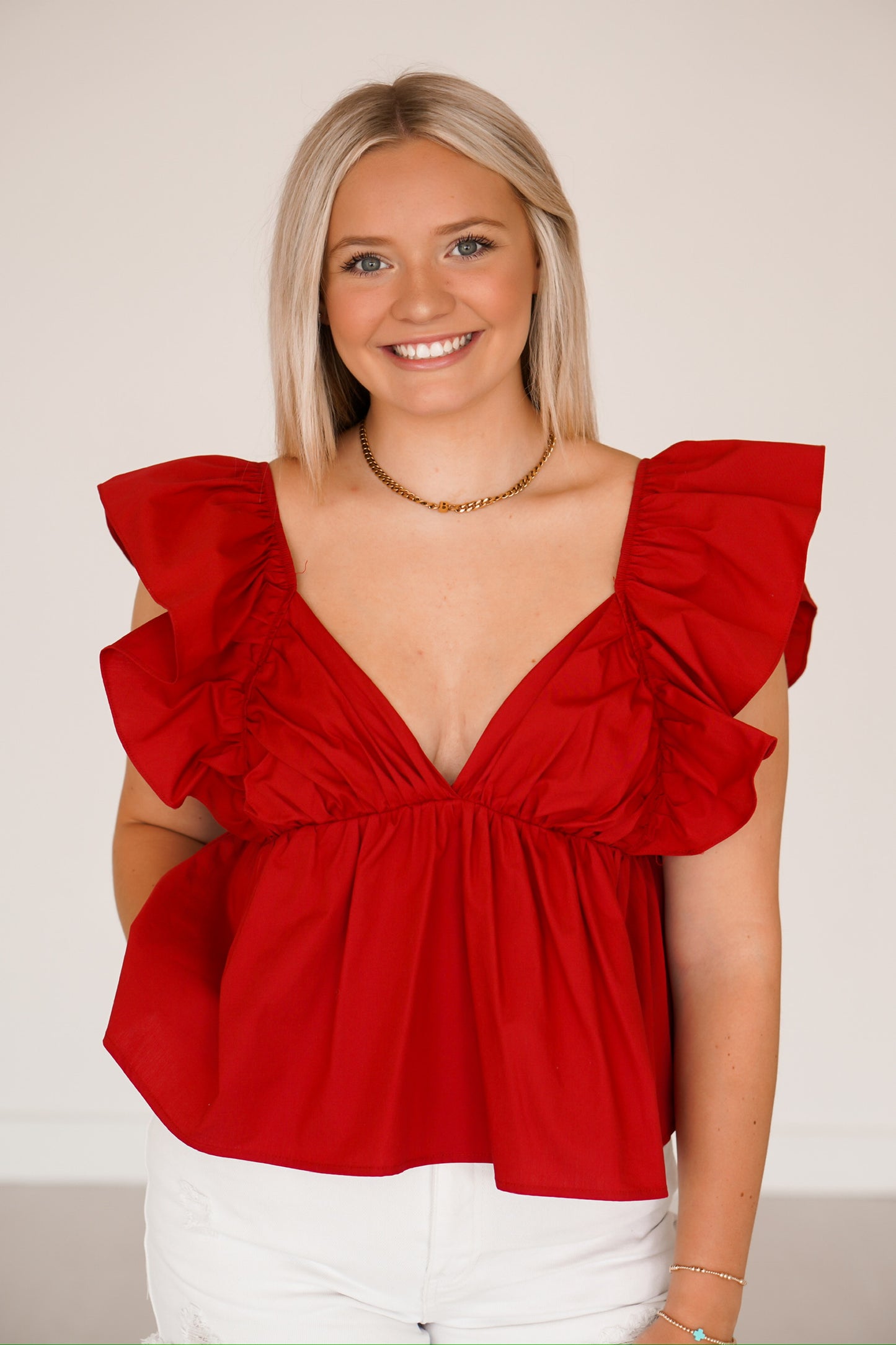 Blonde girl standing against a white wall wearing a crimson red v neck top