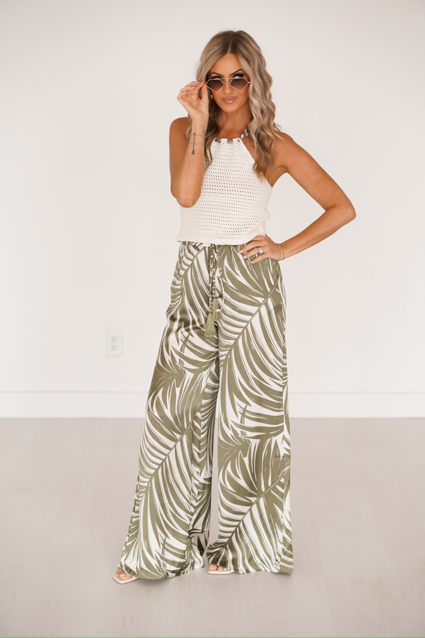 blonde headed girl standing against a white wall wearing a knitted creme palm print top 