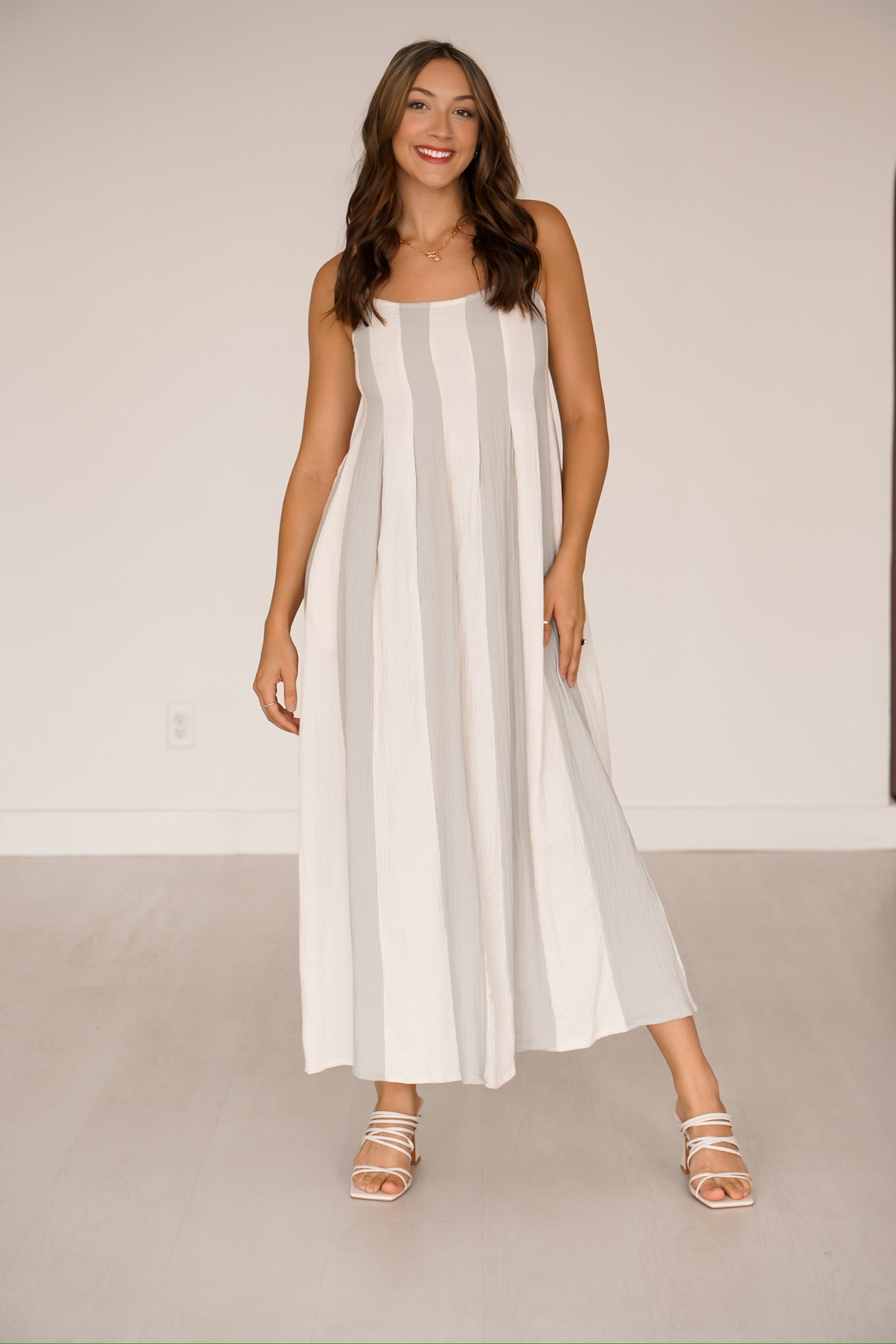 Brunette standing against a white wall wearing a blue and cream striped long dress