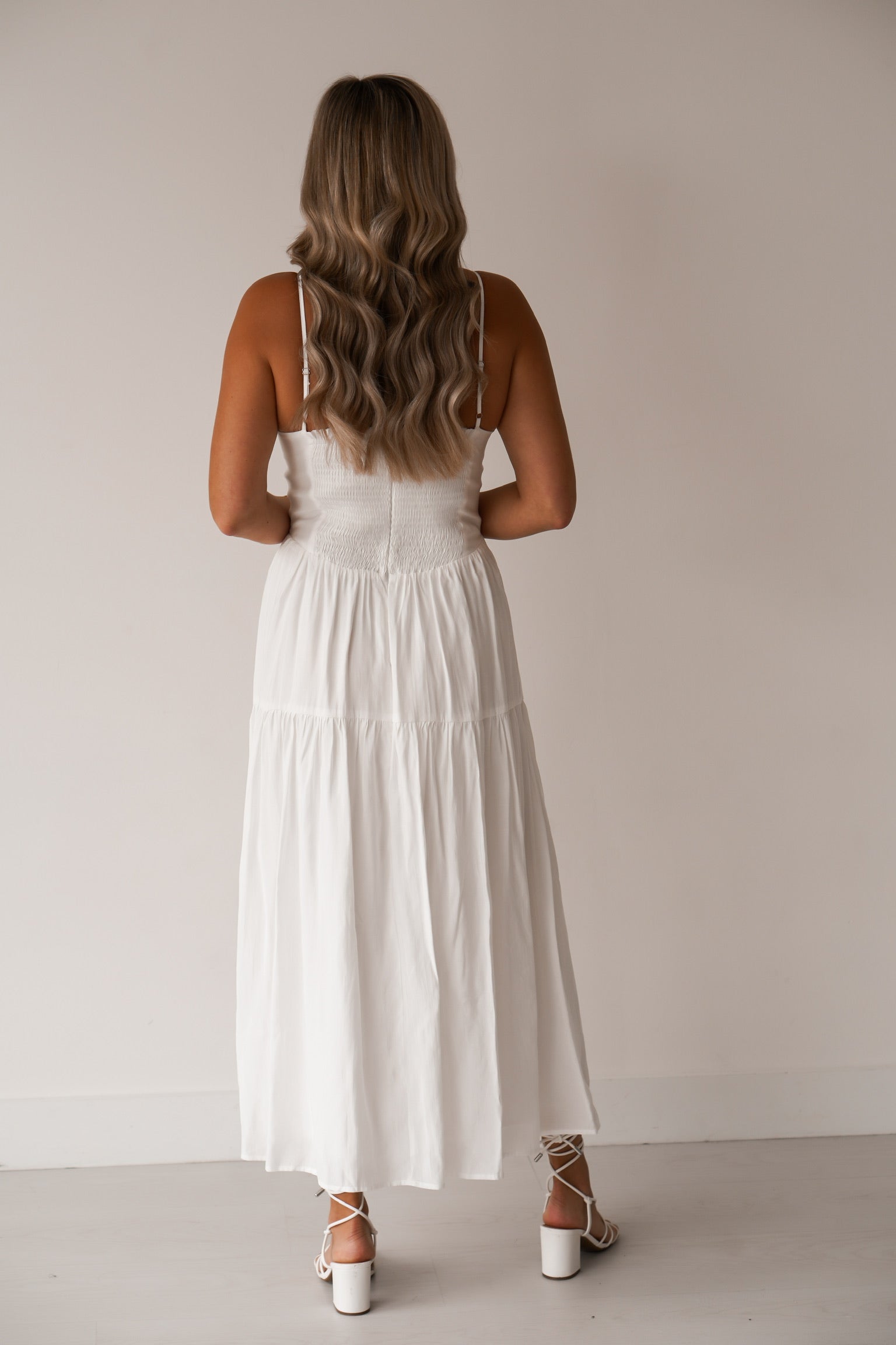 Showing off the back of the white long dress with adjustable straps, a zipper in the back, with smocking 