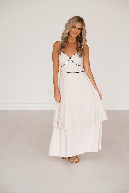 blonde headed lady standing against a white wall wearing a black and creme long maxi dress