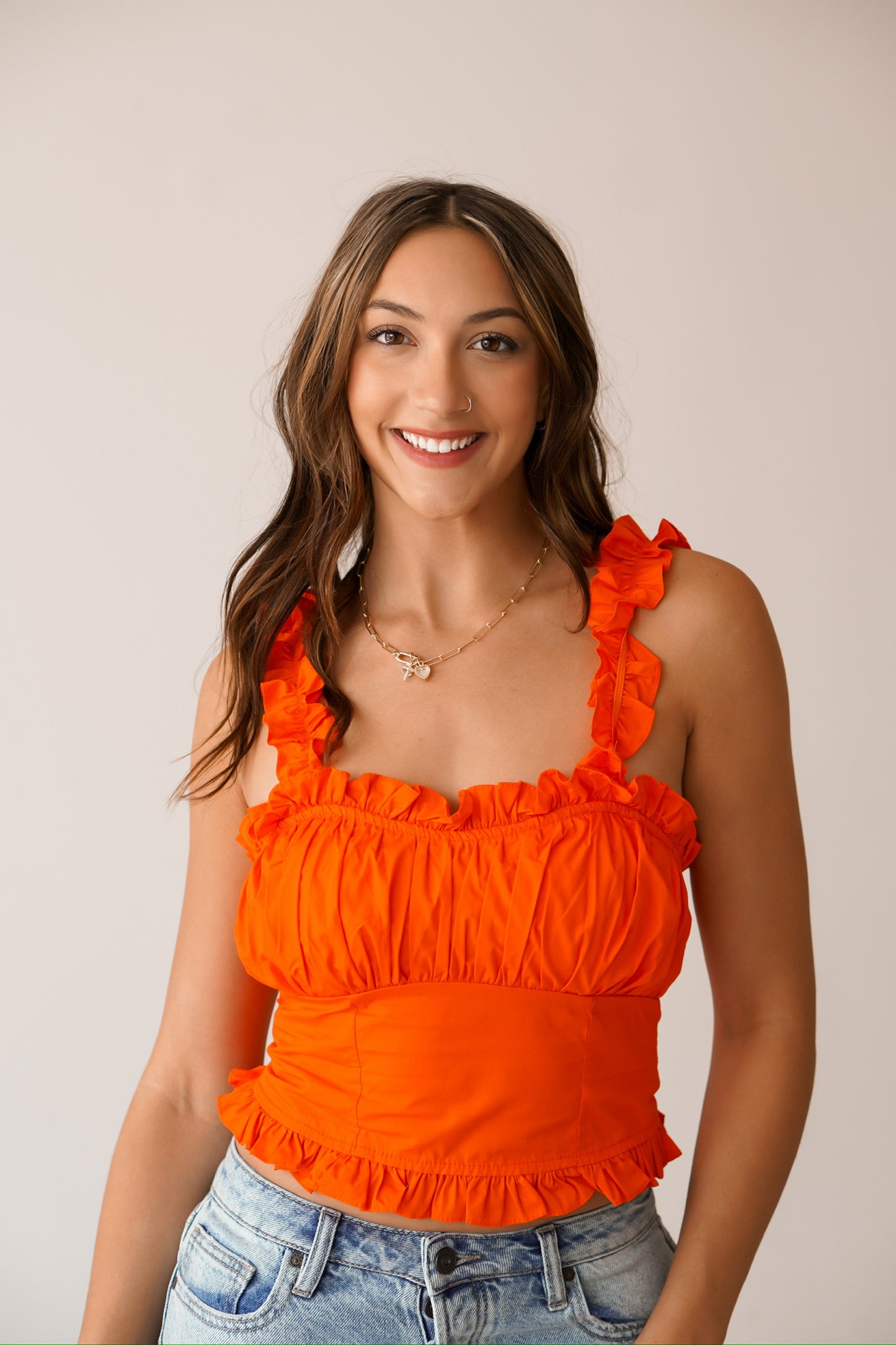 Brunette standing against a white wall wearing a bright orange ruffled top