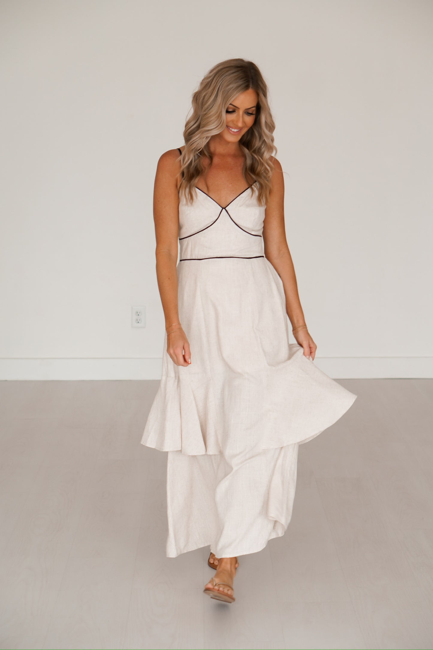 blonde headed lady standing against a white wall wearing a black and creme long maxi dress