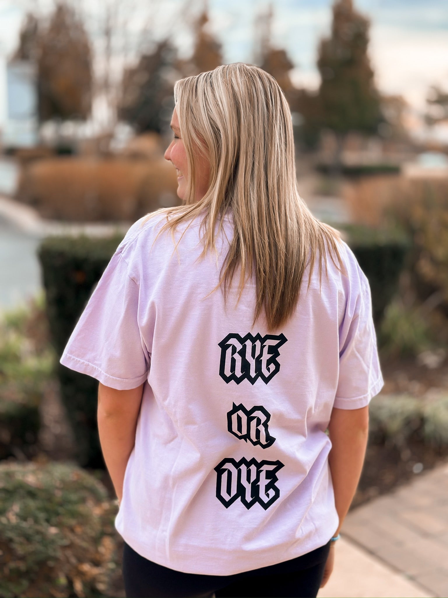 Blonde girl wearing purple short sleeve shirt with RYE OR DYE in black writing on the back. 