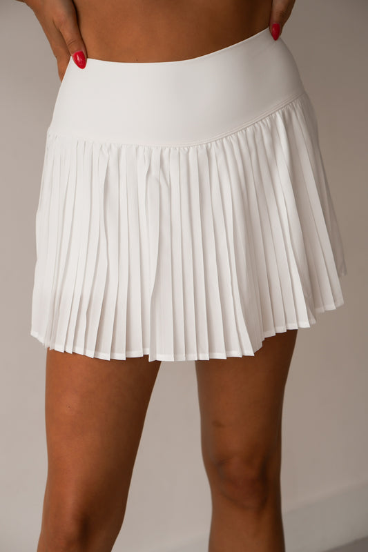 women standing against a white wall with her hands on her hips showing off the front of the pleated white skort 