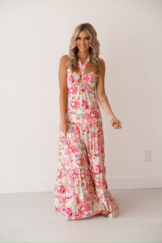 Blonde Girl standing against a white wall with a floral halter dress on. 