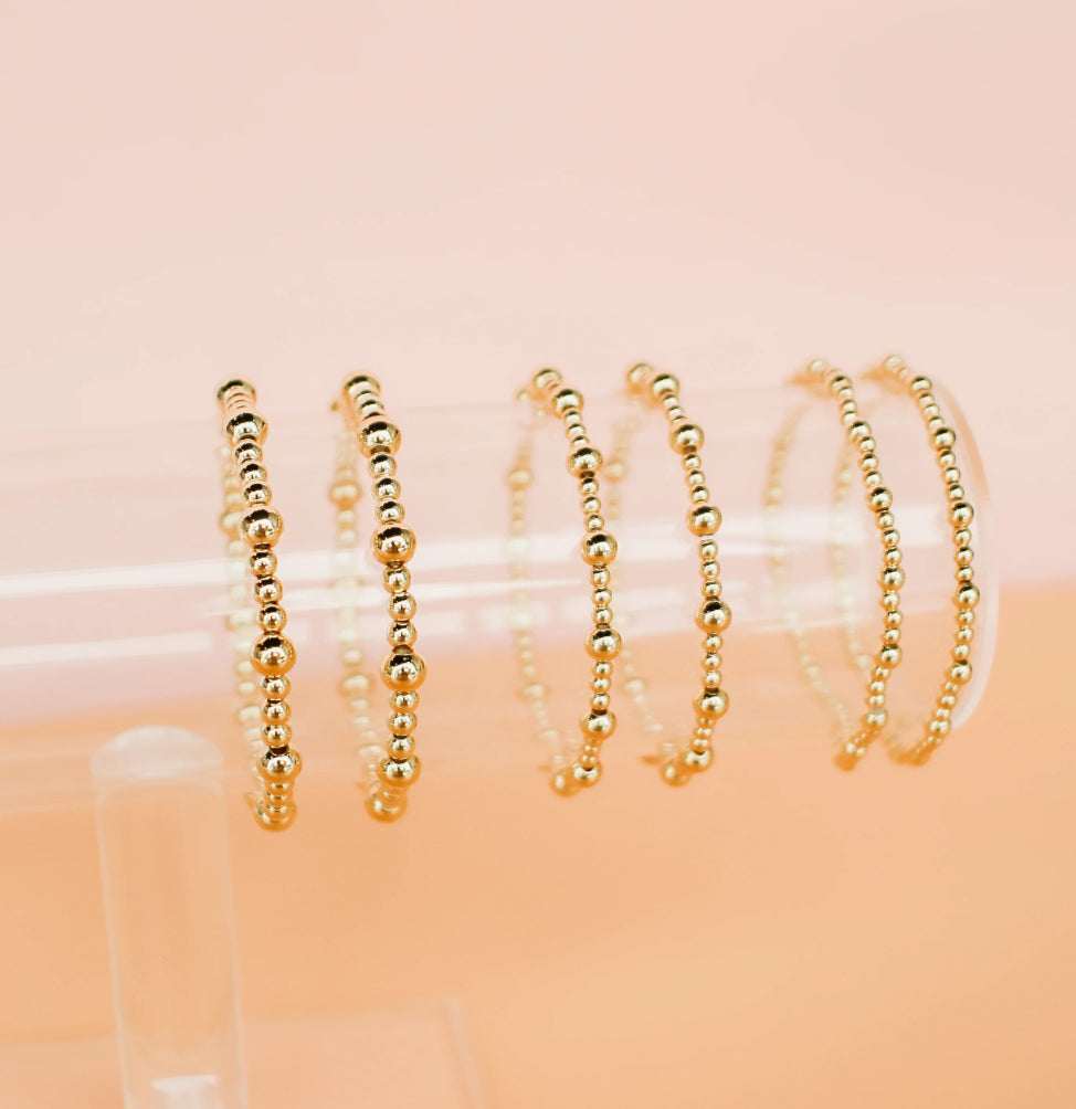gold beaded bracelets stretchy on bracelet stand with pink background