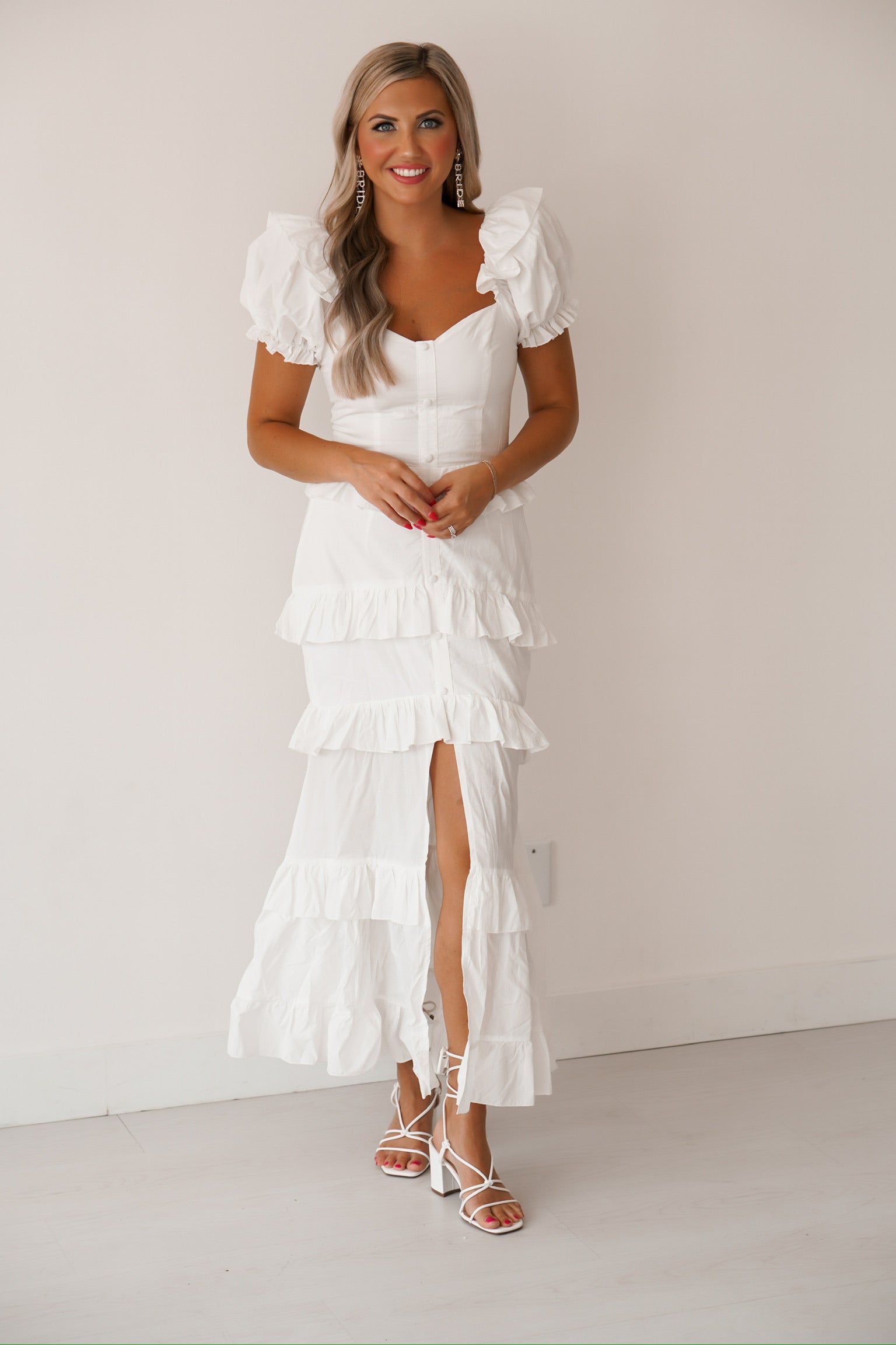 blonde headed girl standing against a white wall wearing a white ruffled maxi dress