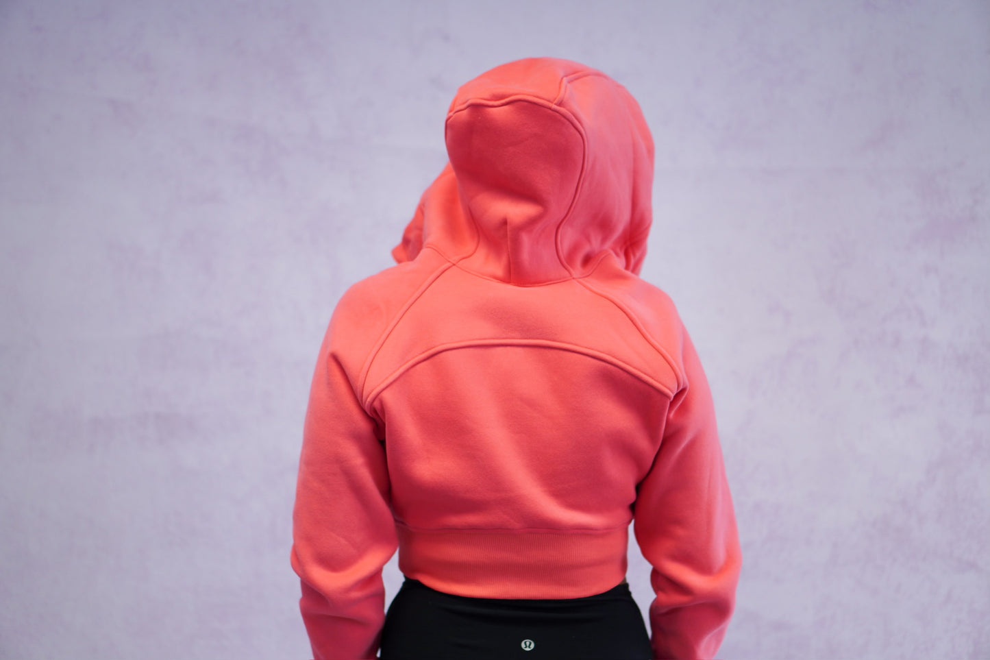 girl facing away from the camera looking back to show the back details of the cropped coral jacket