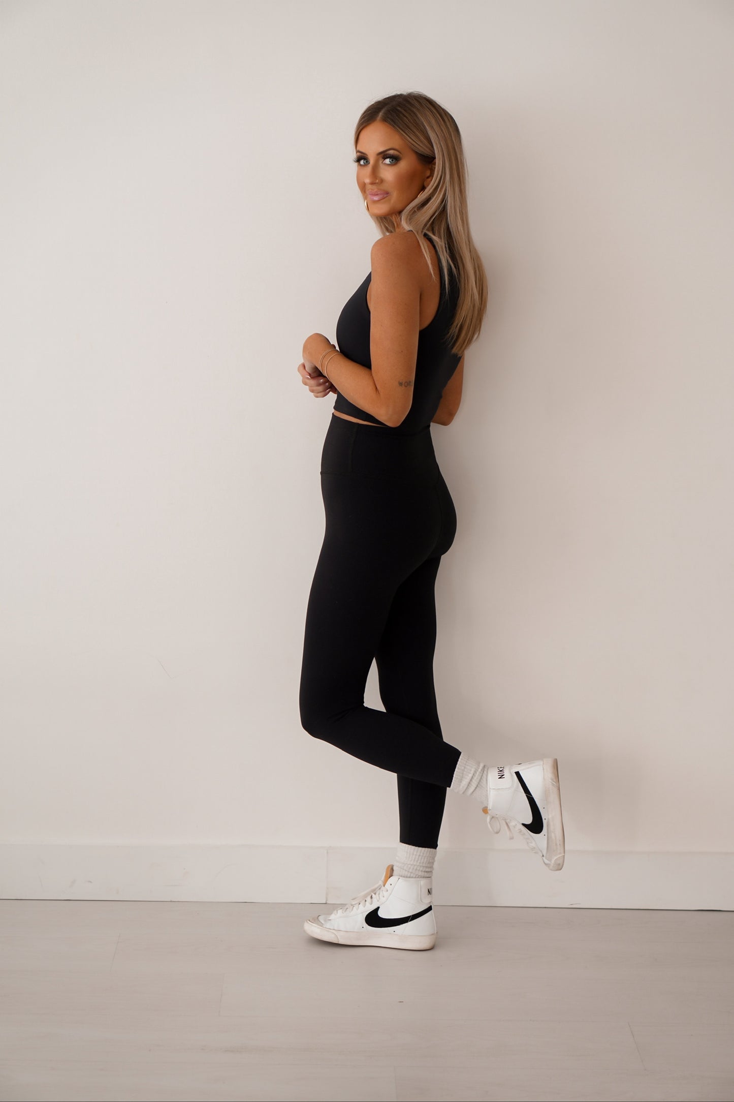 Girl standing in front of white wall showing side view of black workout tank. 