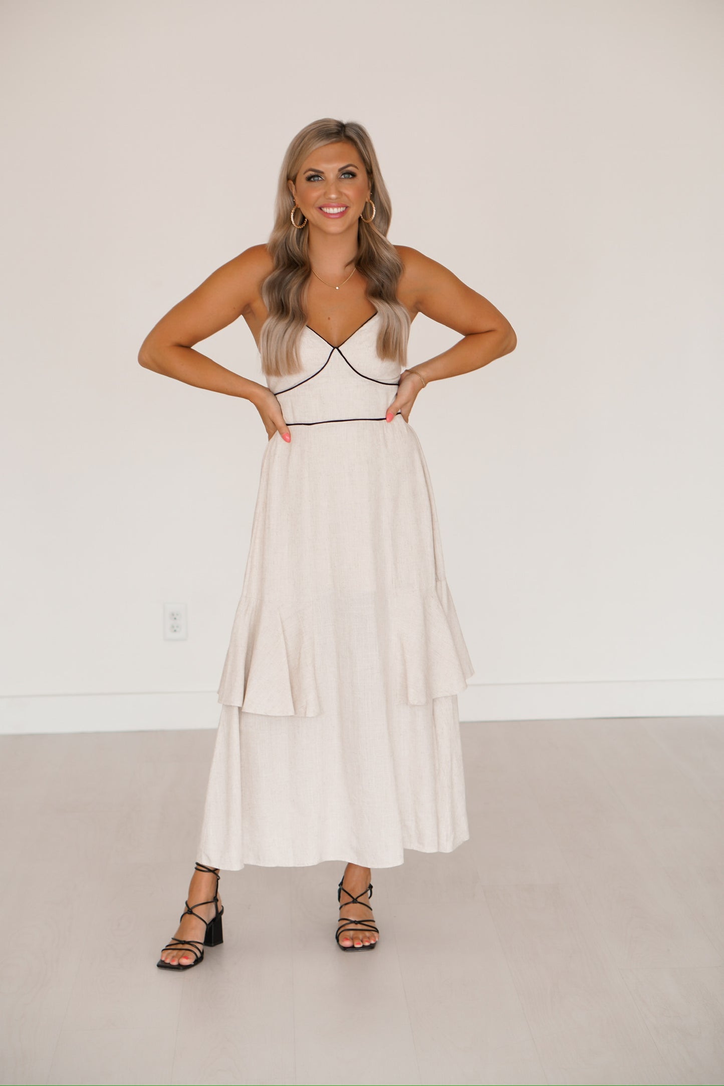 blonde headed lady standing against a white wall wearing a black and creme long maxi dress