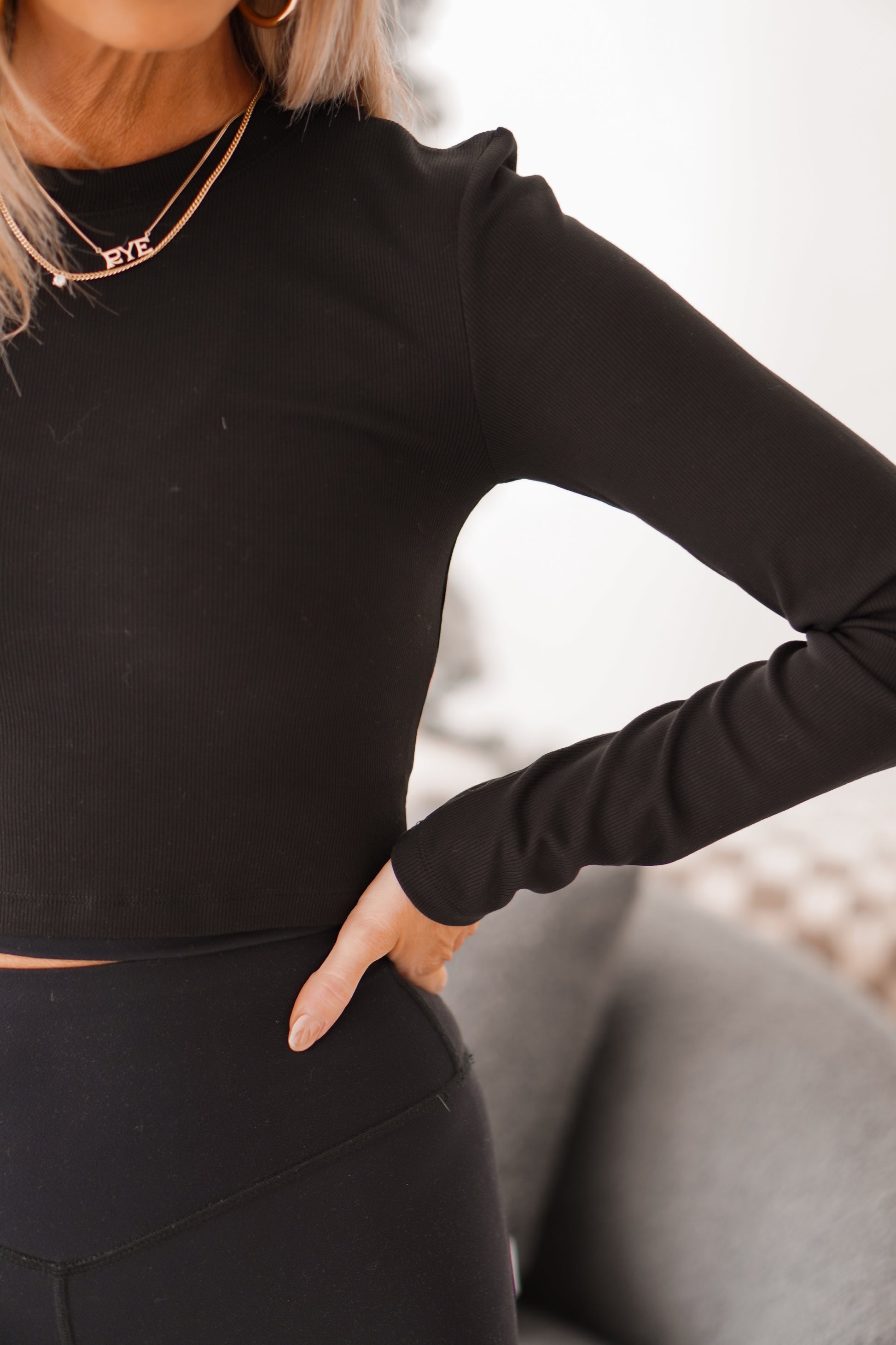 Up close of girl wearing black cropped long sleeve ribbed shirt with hand on hip. 