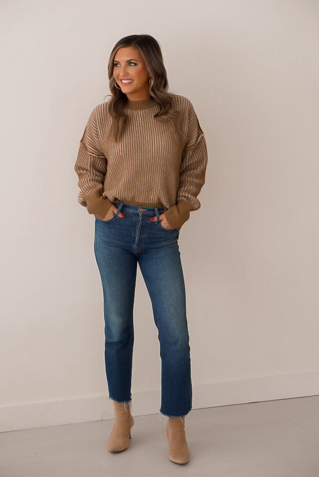 Brunette girl with cream and olive strip sweater. She is standing in front of a white wall.