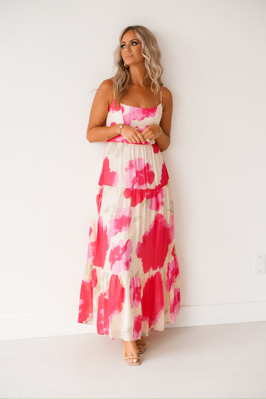 blonde headed lady standing against a white wall wearing a floral pink dress 