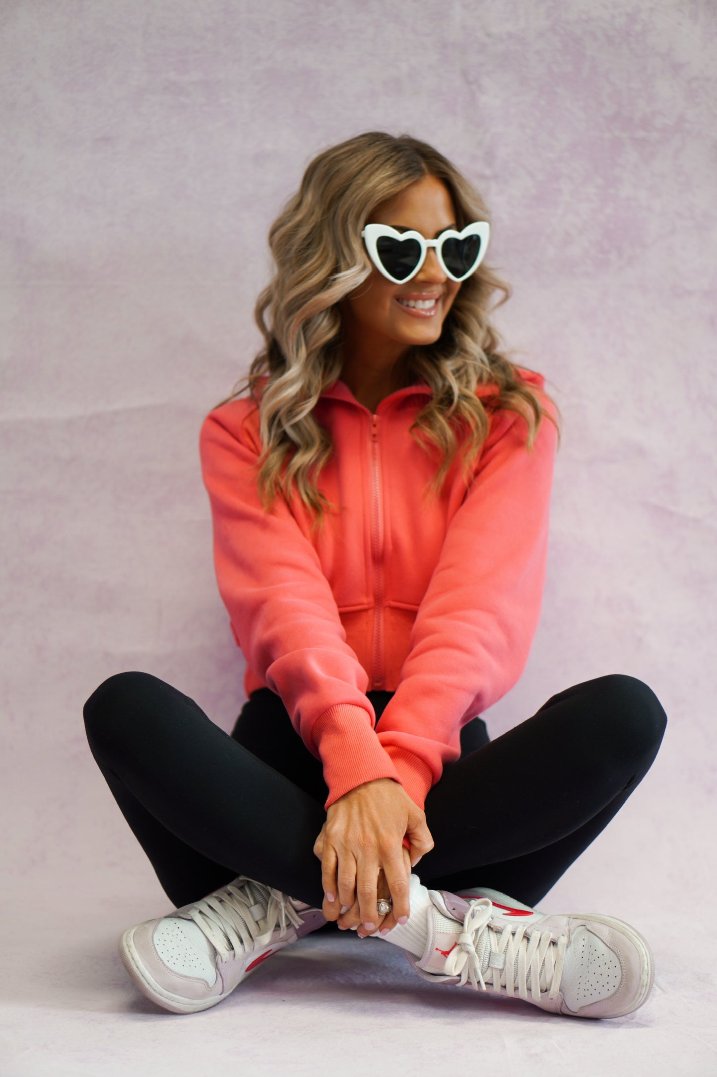 girl sitting wearing cropped coral jacket with heart glasses on wearing nike shoes 