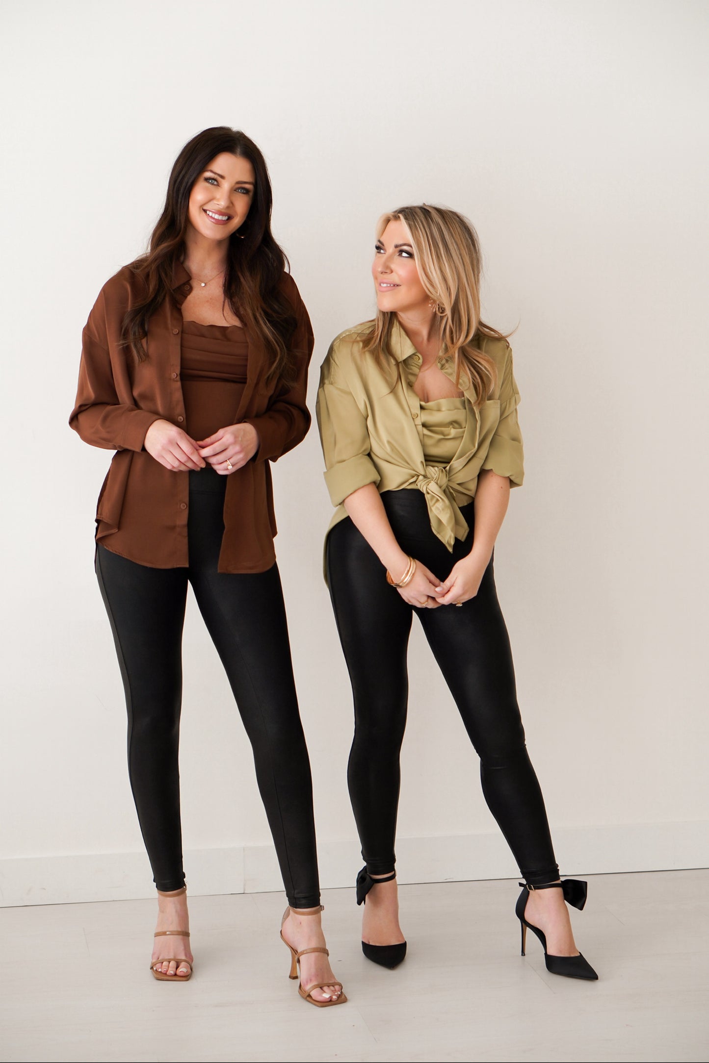 Brunette girl wearing chocolate silk top set with tank and button long sleeve top and a blonde girl wearing the same top in lime, but has it tied up. 
