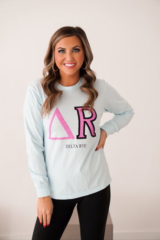 Girl standing with hand on hip wearing blue long sleeve unisex shirt with Greek letters for DELTA RYE. 