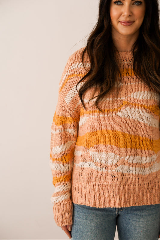 close up shot of sweater that is pink white and orange with a wavy landscape design to it 