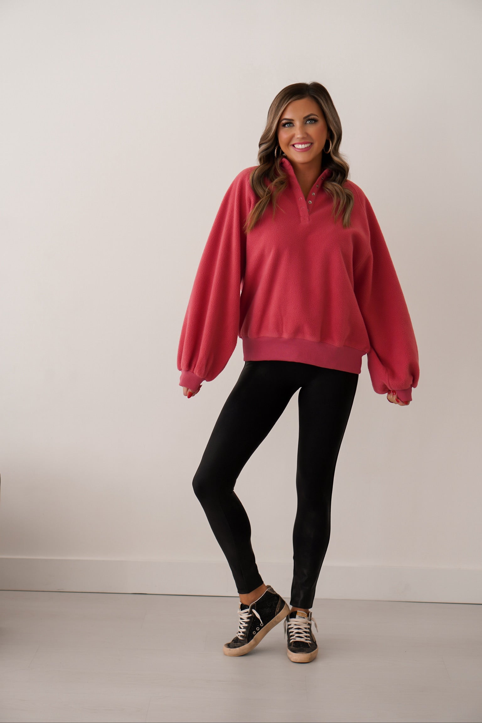 girl standing with arms out to show how sleeves are oversized on this berry color pullover with 1/4 buttons