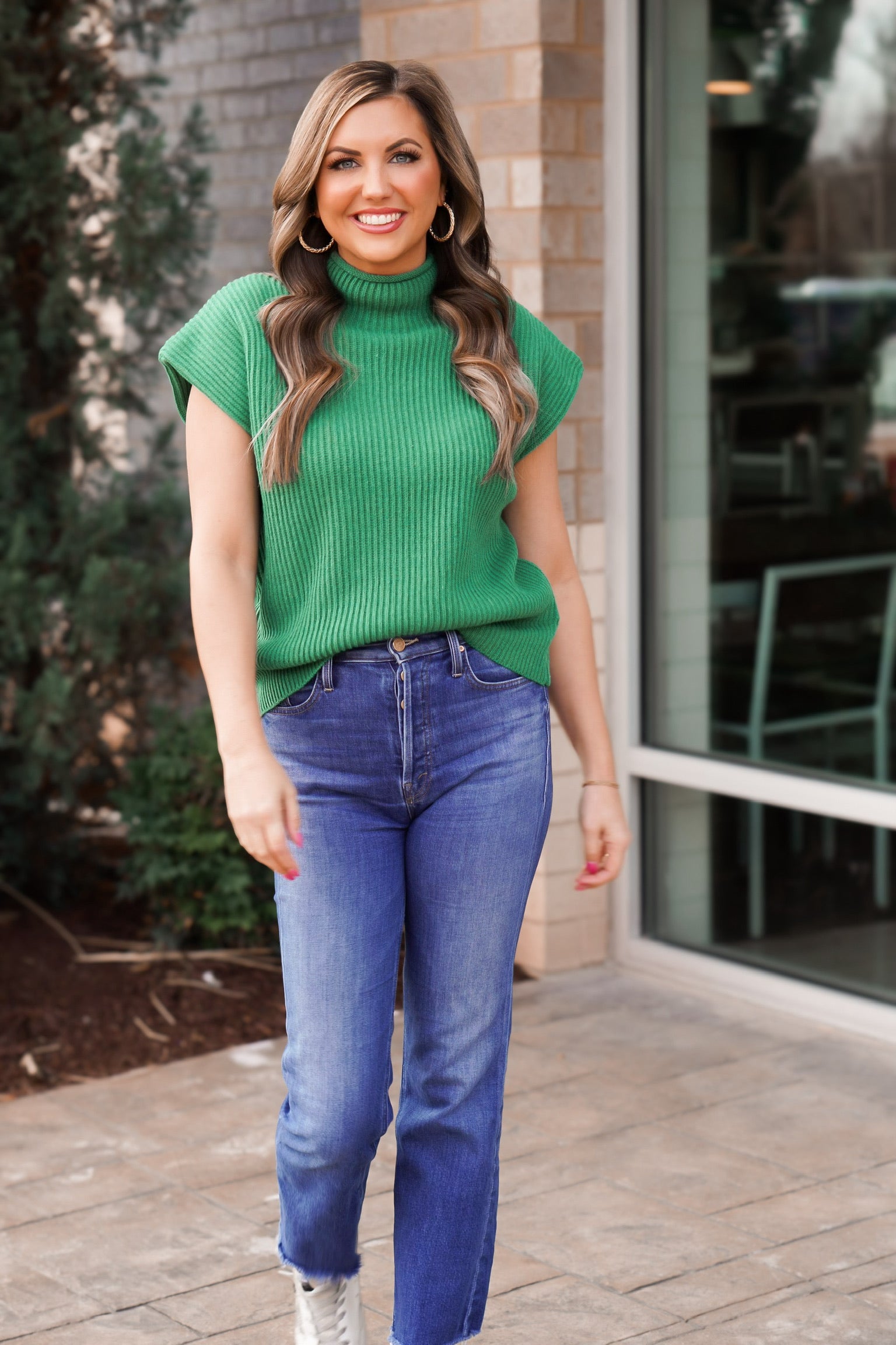girl looking at camera in Kelly green sweater vest with mock neck in jeans