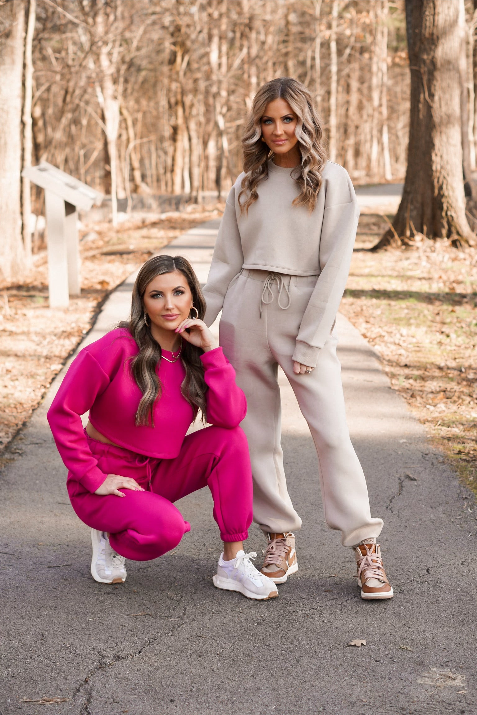 two girls wearing scuba material pullover and joggers. one set being taupe and the other pink. one girl is kneeling down posing while the other girl is standing 
